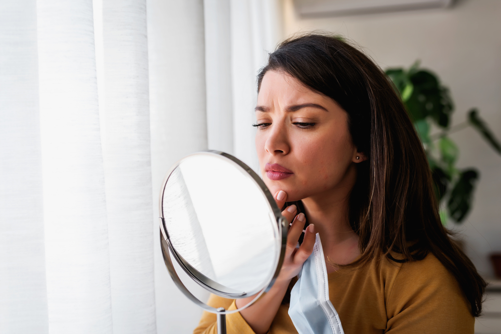 Woman looks at a chin scar in a handheld mirror before scar revision surgery