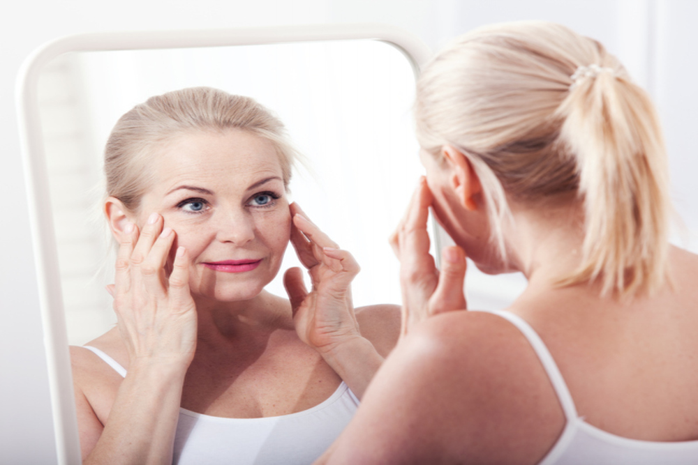 Woman touches her face, looking in the mirror and thinking about which anti-aging treatment to get