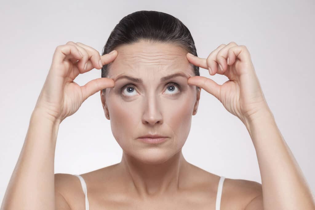Middle-aged woman pinching her brow area, in need of either Botox or a brow lift. Middle-aged woman pinching her brow area, in need of either Botox or a brow lift.